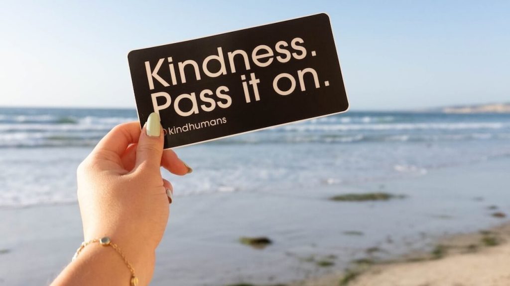 Person holding a card reading "Kindness. Pass it on." promoting acts of kindness messages